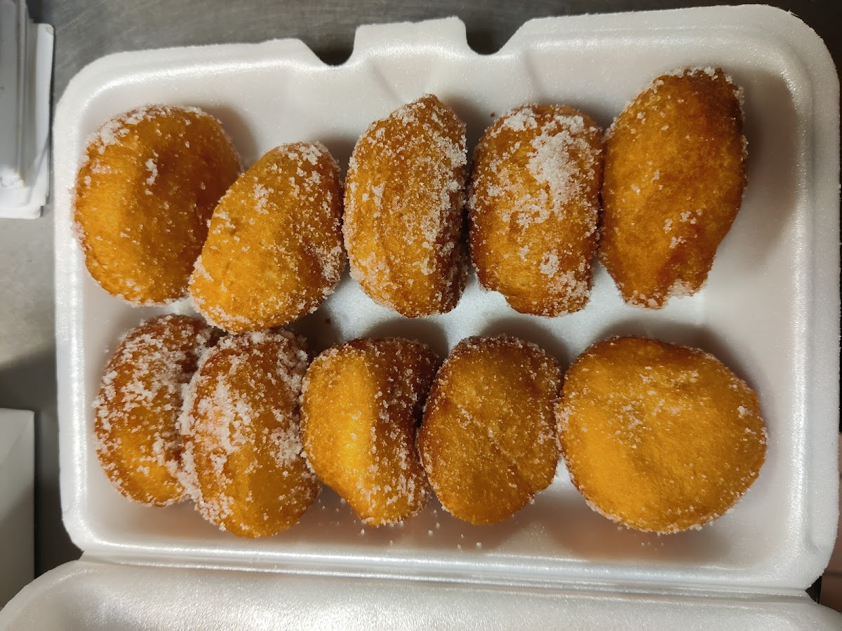 Ten golden Chinese sugar donuts dusted in sugar in a styrofoam container
